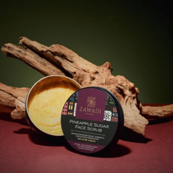 Open jar of Pineapple, Camwood & Turmeric Sugar Scrub on a wooden stick, showing rich texture and golden hue