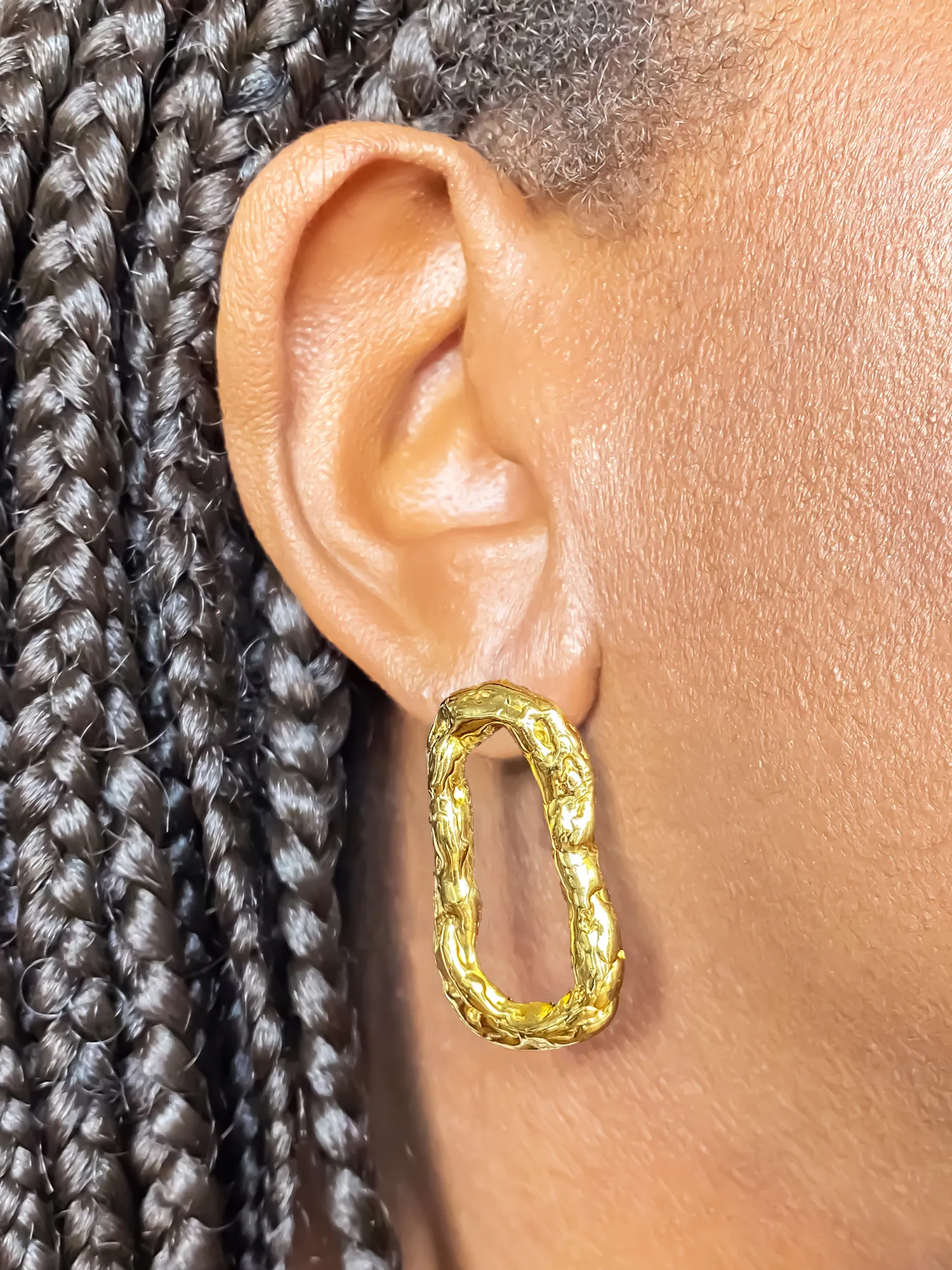 Close-up of gold Flow Loop Earrings worn on ear, featuring flowing design