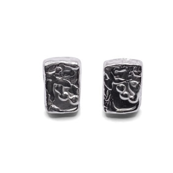 Detailed close-up of rectangular sculpted silver earrings with organic texture