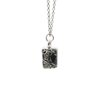 Silver chain necklace with rectangular sculpted pendant flat lay photography