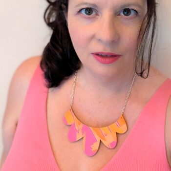 Handmade statement necklaceon bold pink and orange abstract design. Shown worn with a pink top against a cream background to emphasise the necklace and it's striking colourful design